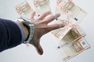 A hand reaching towards a pile of money notes