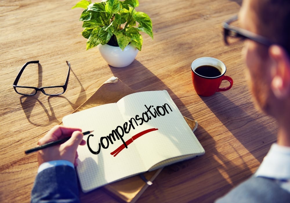 A person at a desk, with a notebook with the word "Compensation" written in large letters