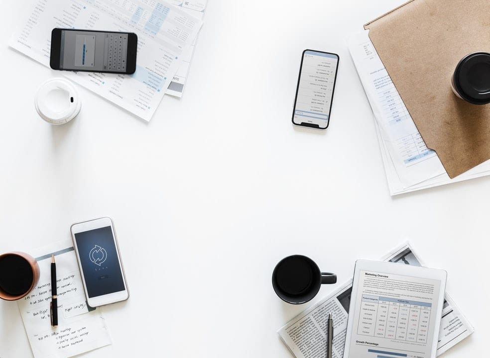 A business meeting desk with a collection of beverages, notebooks and pens on it